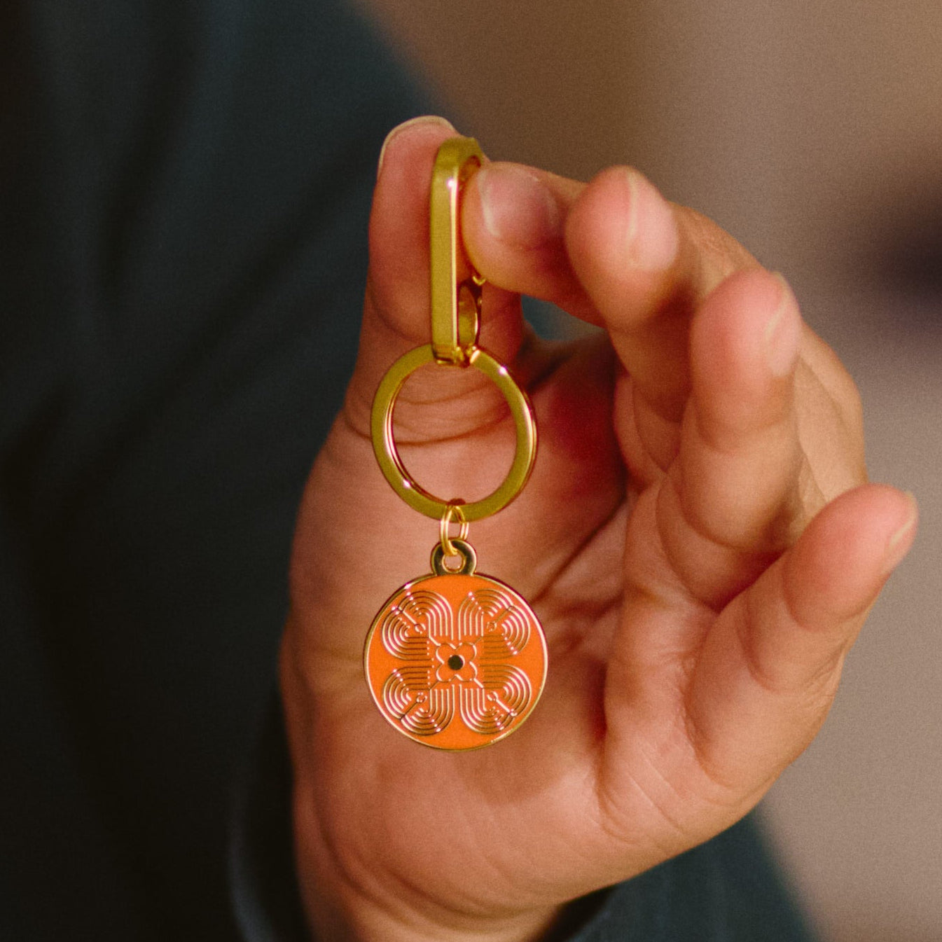 Hand holding a gold keychain with an orange pendant against a blurred background