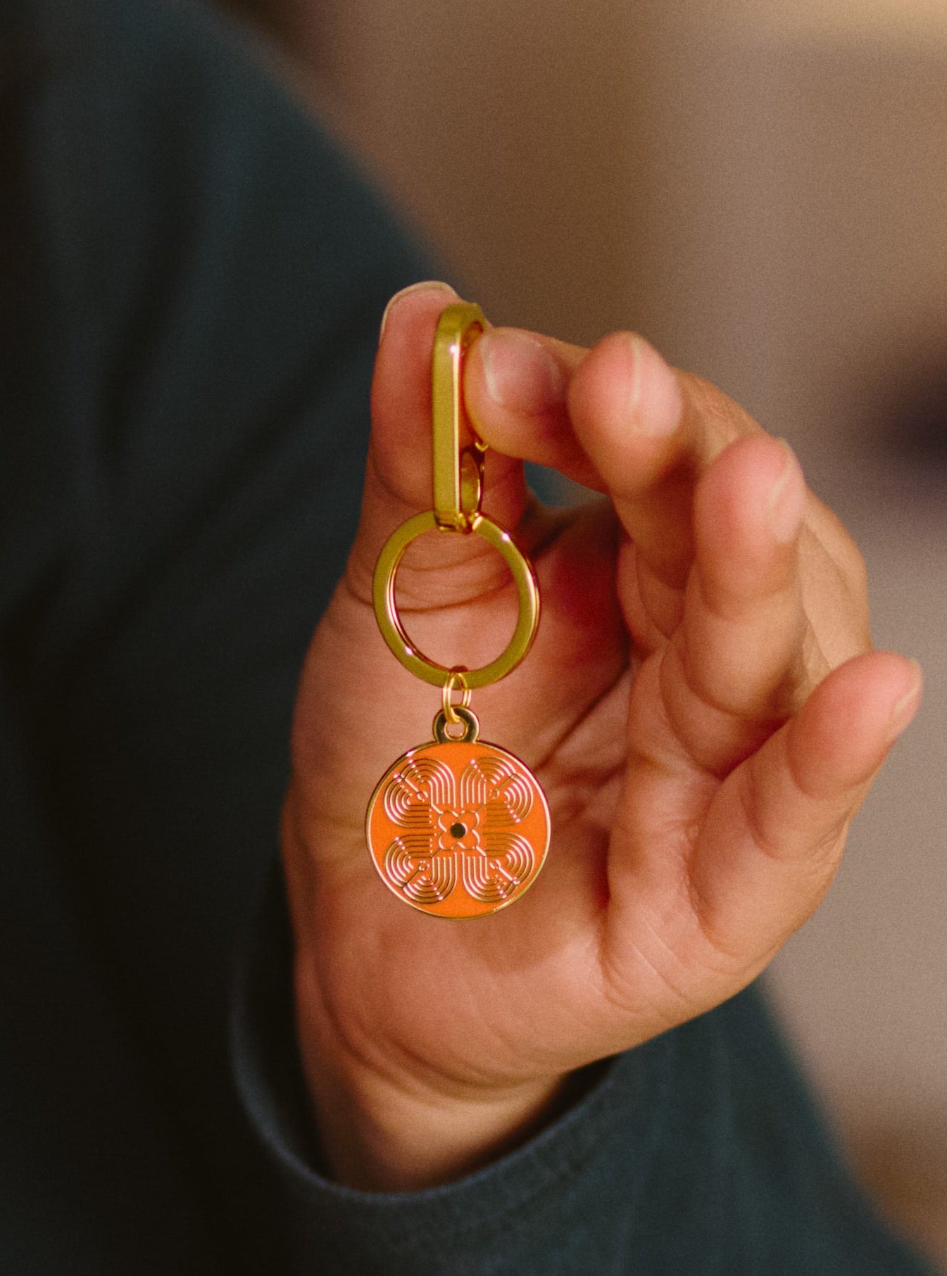 Hand holding a gold keychain with an orange pendant against a blurred background